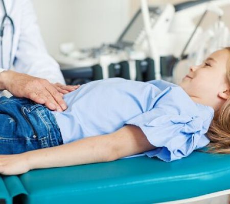 Unrecognizable doctor palpating belly of little girl lying on couch in doctors office and smiling