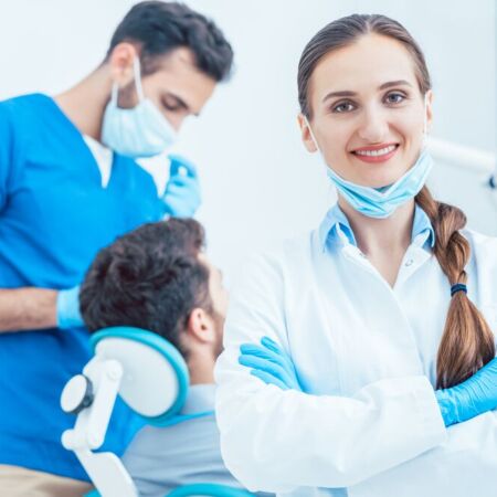 Portrait of a happy and confident female dentist wearing sterile white coat and surgical gloves, while looking at camera in the dental office of a modern clinic with reliable specialists
